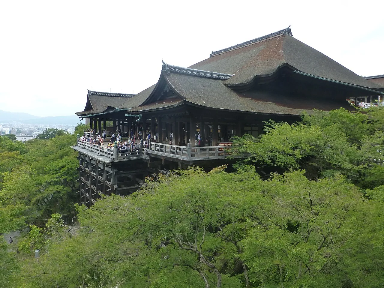 Kiyomizu-dera temple's wooden main hall above green trees in Kyoto, Japan.